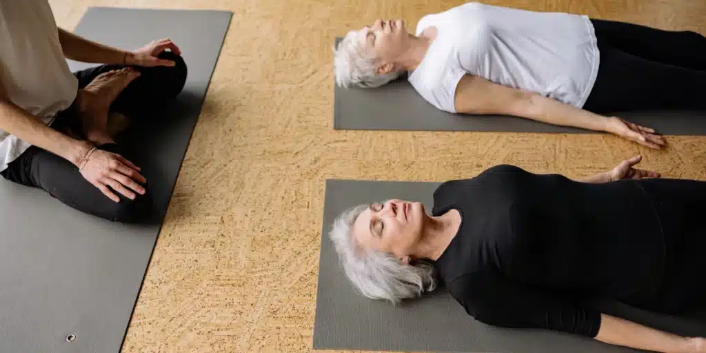 3 older persons laying on mats being mindful. 